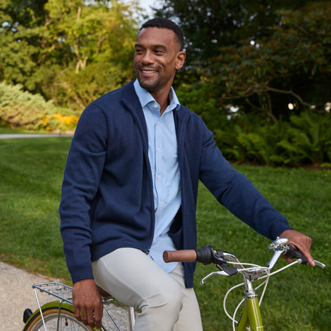 A cyclist in an open navy full-zip sweater over a light blue shirt, beside a bike in a park.