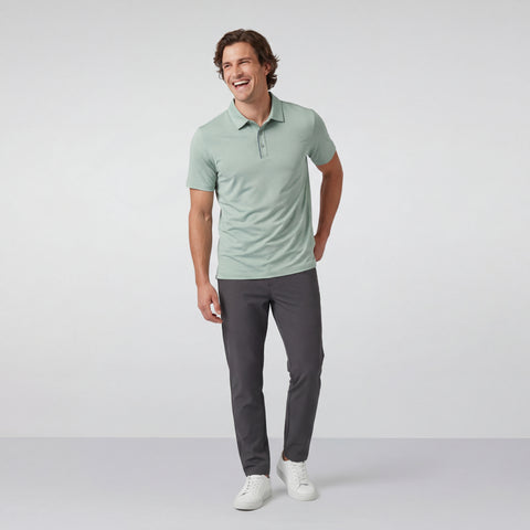 Man wearing a light green polo shirt and dark gray pants on a white background