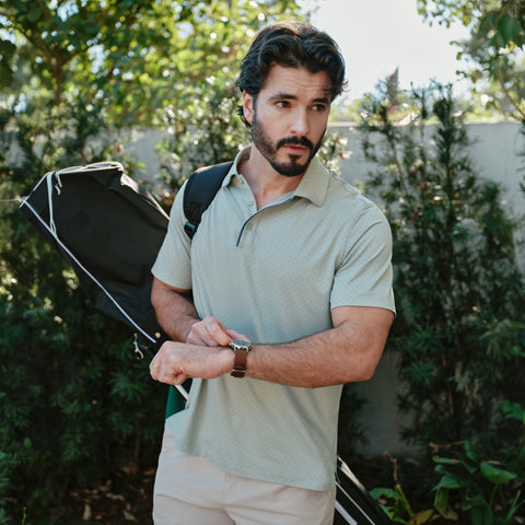 Man holding a golf bag outdoors with greenery in the background