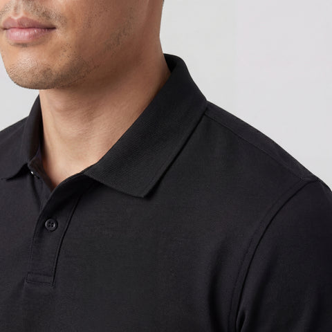 Close-up of a person wearing the Jack Archer Clubhouse Pique Polo in True Black, featuring a collared design with buttons, showing the lower half of their face and upper torso against a plain background.