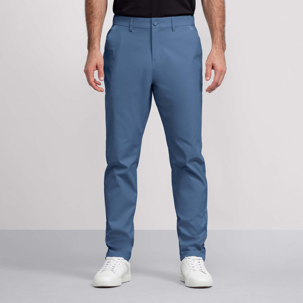 A person stands against a plain light background, shown from shoulders to feet, wearing Jack Archer’s Jetsetter Tech Pant in light blue (slim-fit, wrinkle-resistant), paired with a black shirt and white sneakers.
