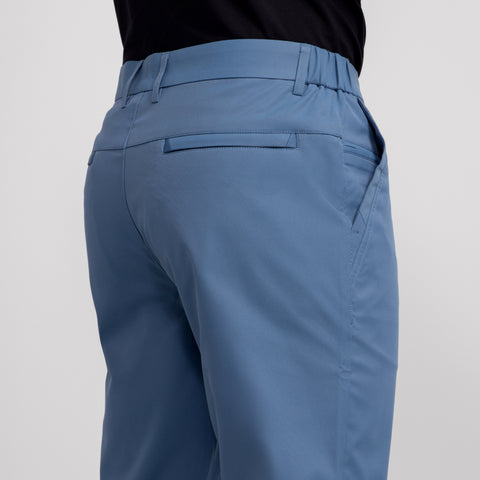A person is shown from the back wearing Jetsetter Tech Pant Slim Fit in light blue, featuring a wrinkle-free design and visible waistband and pockets, paired with a black shirt.