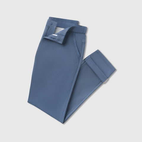 A pair of Jetsetter Tech Pant Slim Fit in blue, neatly folded with the button and zipper partially undone, displayed on a plain light gray background.