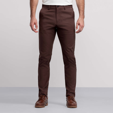 A man wears Jack Archer Jetsetter Tech Pant 3-Pack in brown, paired with a white shirt and brown leather shoes, standing against a light gray background. The image captures him from the chest down with his arms at his sides.