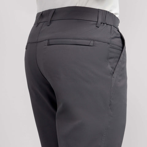 A close-up of the back and side of a person wearing Jetsetter Tech Pant Slim Fit in dark gray with wrinkle-free fabric, featuring a waistband, welt back pocket, and side pocket, paired with a white shirt against a plain background.