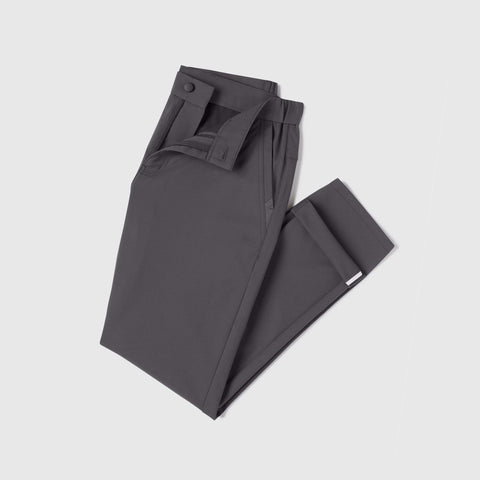 A pair of Jetsetter Tech Pant Slim Fit in dark gray, wrinkle-free with matching fabric belt, neatly folded and displayed on a light gray background.
