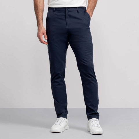 A man models the Jetsetter Tech Pant Straight Fit in navy blue against a plain background, paired with a white shirt and white sneakers. Only his lower body and part of his torso are visible.