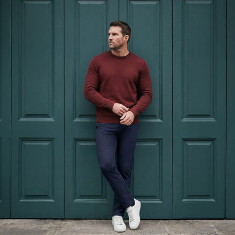 Navy Jetsetter pants and a burgundy crewneck sweater, worn against a dark green panelled door.