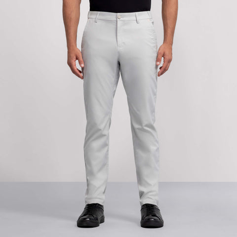 A person wears light gray Jack Archer Jetsetter Tech Pant, a black shirt, and black shoes, standing facing forward against a plain gray background.