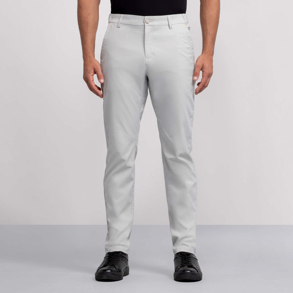 A person wears light gray Jack Archer Jetsetter Tech Pant, a black shirt, and black shoes, standing facing forward against a plain gray background.
