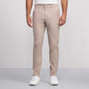 A person wears Jack Archer's Jetsetter Tech Pant Slim Fit in Oak Khaki with white sneakers, standing against a plain light gray background. Only their lower torso and legs are visible; the upper body is mostly out of frame.