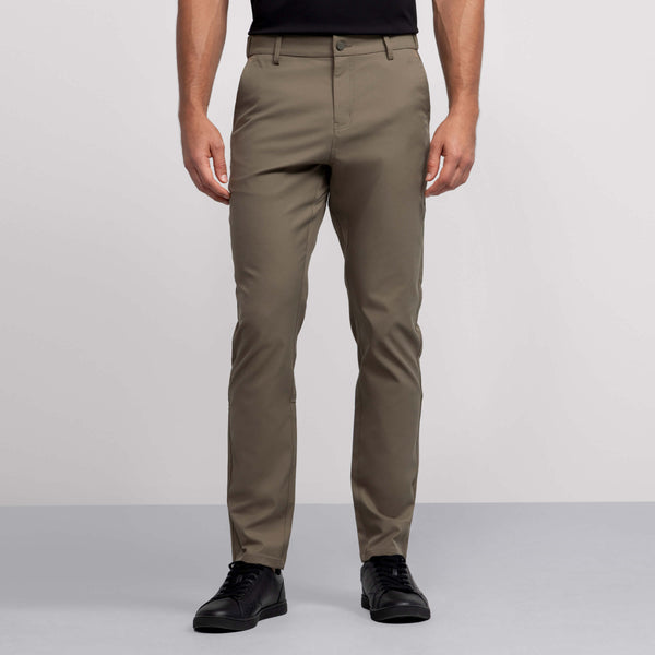 Wearing Jack Archer's wrinkle-resistant olive green Jetsetter Tech Pant, a person—upper body not visible—stands in black shirt and sneakers against a plain light grey background.