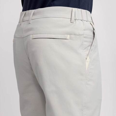 A person wears Jack Archer Jetsetter Tech Pant Straight Fit in Sand Stone, featuring belt loops, welt back pockets, and a smooth finish; shirt tucked in, shown waist down from behind.
