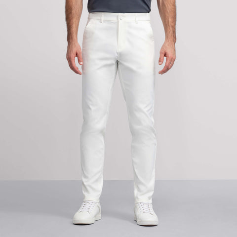 A person wearing white Jack Archer Jetsetter Tech Pant with white sneakers and a dark shirt stands against a light gray background, showing only the lower half of the body.