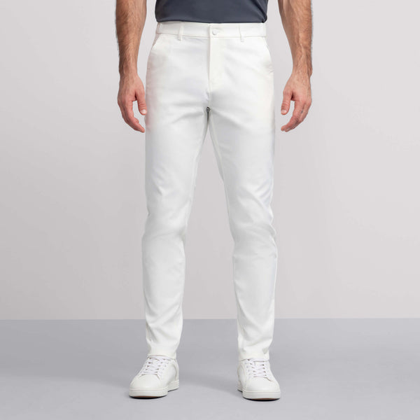 A person wearing white Jack Archer Jetsetter Tech Pant with white sneakers and a dark shirt stands against a light gray background, showing only the lower half of the body.