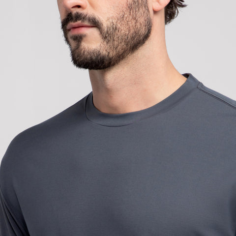 A man with a trimmed beard models the Jack Archer Jetsetter Tee in Charcoal Gray, crewneck style. Shown from the shoulders up against a light gray background, his face partially out of frame adds a subtle travel-ready vibe.