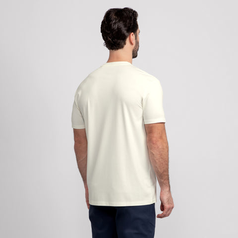 A man with short dark hair, seen from behind, wears a plain ecru Jack Archer Jetsetter Tee and dark pants, standing against a light gray background.