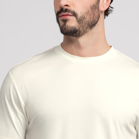 A man with a short beard wears the Jack Archer Jetsetter Tee in Ecru, shown from the shoulders up with his face turned slightly to the side against a plain light gray background.