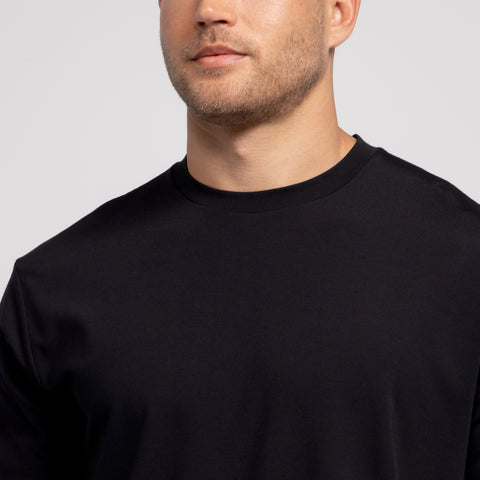 A man with light skin and short facial hair models the Jack Archer Jetsetter Tee in True Black, a plain crewneck t-shirt, shown from the shoulders up against a neutral background, his face partially visible as he looks slightly aside.