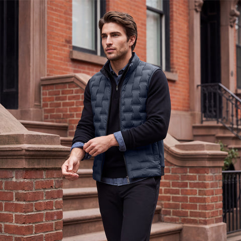 A man in the deep blue quilted Drive vest walking past a brownstone stoop.