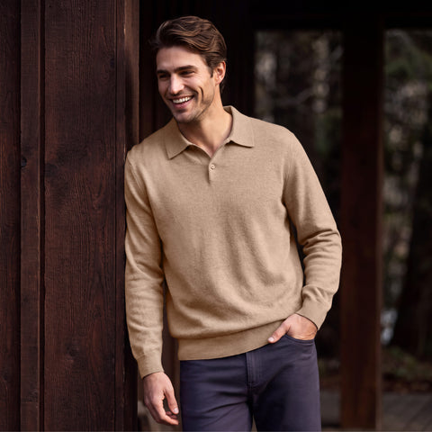 A man in a mocha heather long-sleeve knit polo leaning against a dark wood wall.