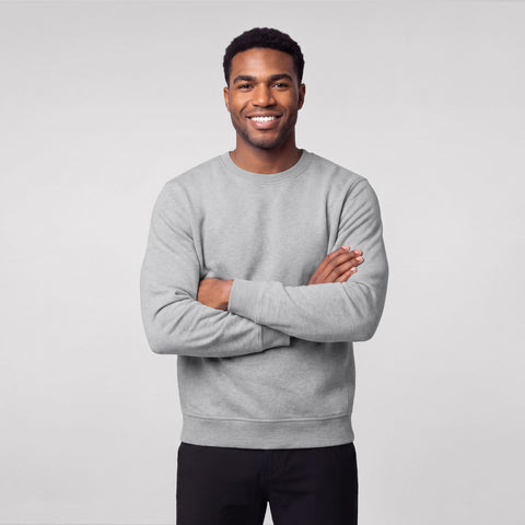 A man in a heather gray crewneck sweatshirt and black pants, arms crossed.