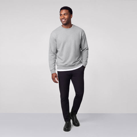 A man in a heather gray crewneck sweatshirt over a white tee with black pants and boots.