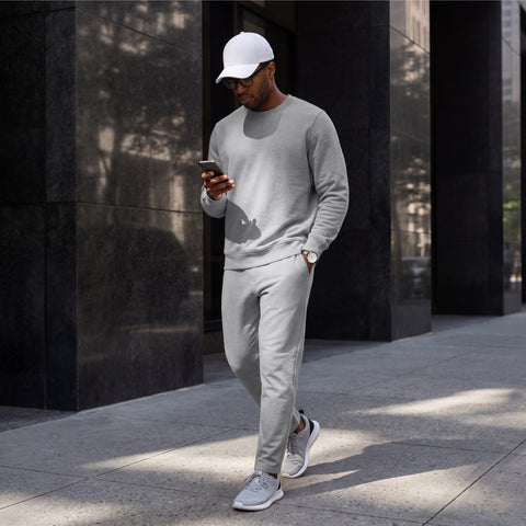 A man in a heather gray crewneck sweatshirt and matching sweatpants walking down a city street.