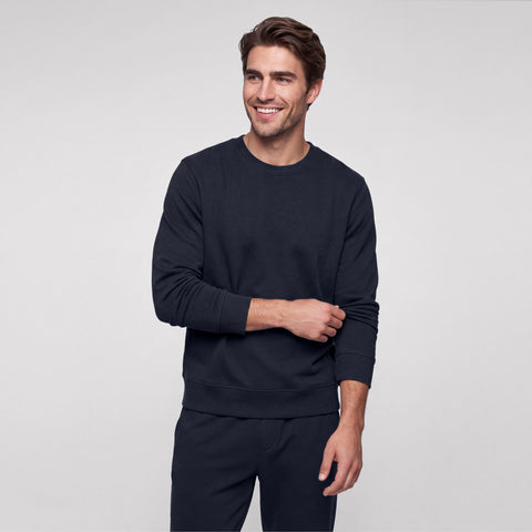 A man in a midnight navy crewneck sweatshirt and matching sweatpants, hand on sleeve.