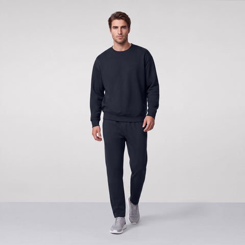 A man in a midnight navy crewneck sweatshirt and matching sweatpants with gray sneakers.