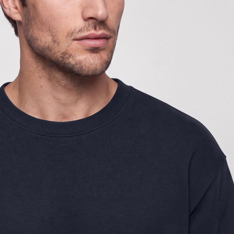 Close-up of a midnight navy crewneck sweatshirt's ribbed collar and shoulder seam.