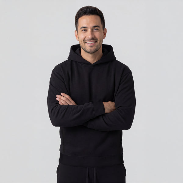 Man wearing a black hoodie with arms crossed on a light gray background